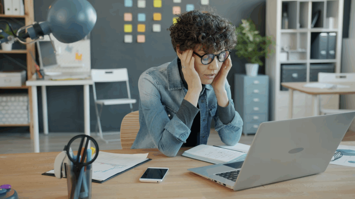 Une femme devant son bureau se prend la tête.
