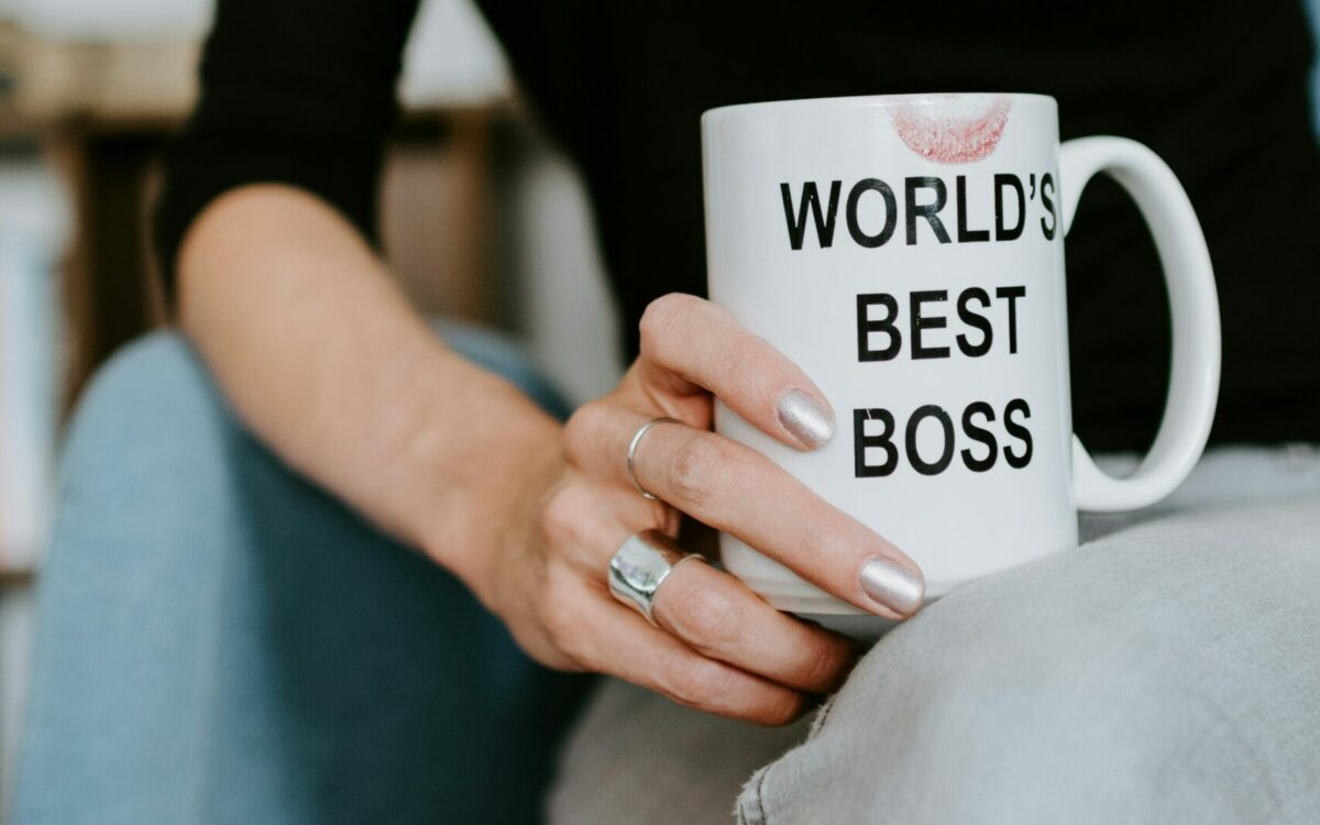 Main de femme tenant une tasse sur laquelle on peut lire "World's best boss" avec une trace de rouge à lèvres.