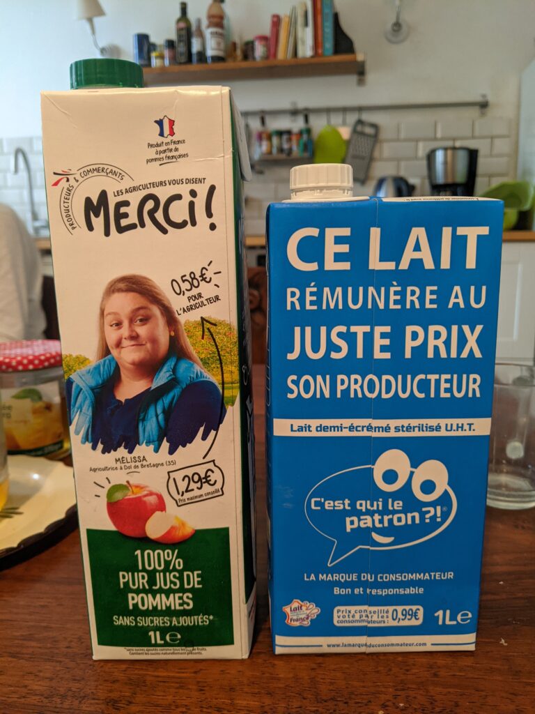 Un photo d'une brique de jus de pomme de la marque "Les agriculteurs vous disent merci !" où l'on voit le portrait d'une agricultrice, et d'une brique de lait "C"est qui le patron ?!" où il est écrit "Ce lait rémunère au juste prix son producteur"