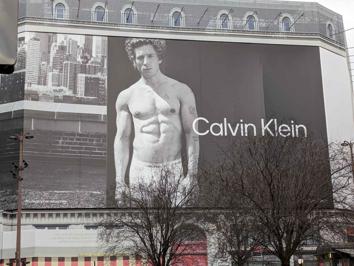 Photo d'une immense affiche recouvrant un immeuble parisien où l'on voit l'acteur Jérémy Allen White torse nu pour promouvoir les sous-vêtements de la marque Calvin Klein.